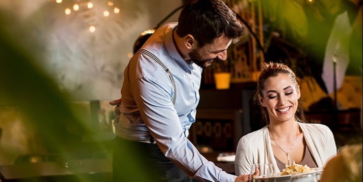Waiter serving food to female customer in a restaurant.